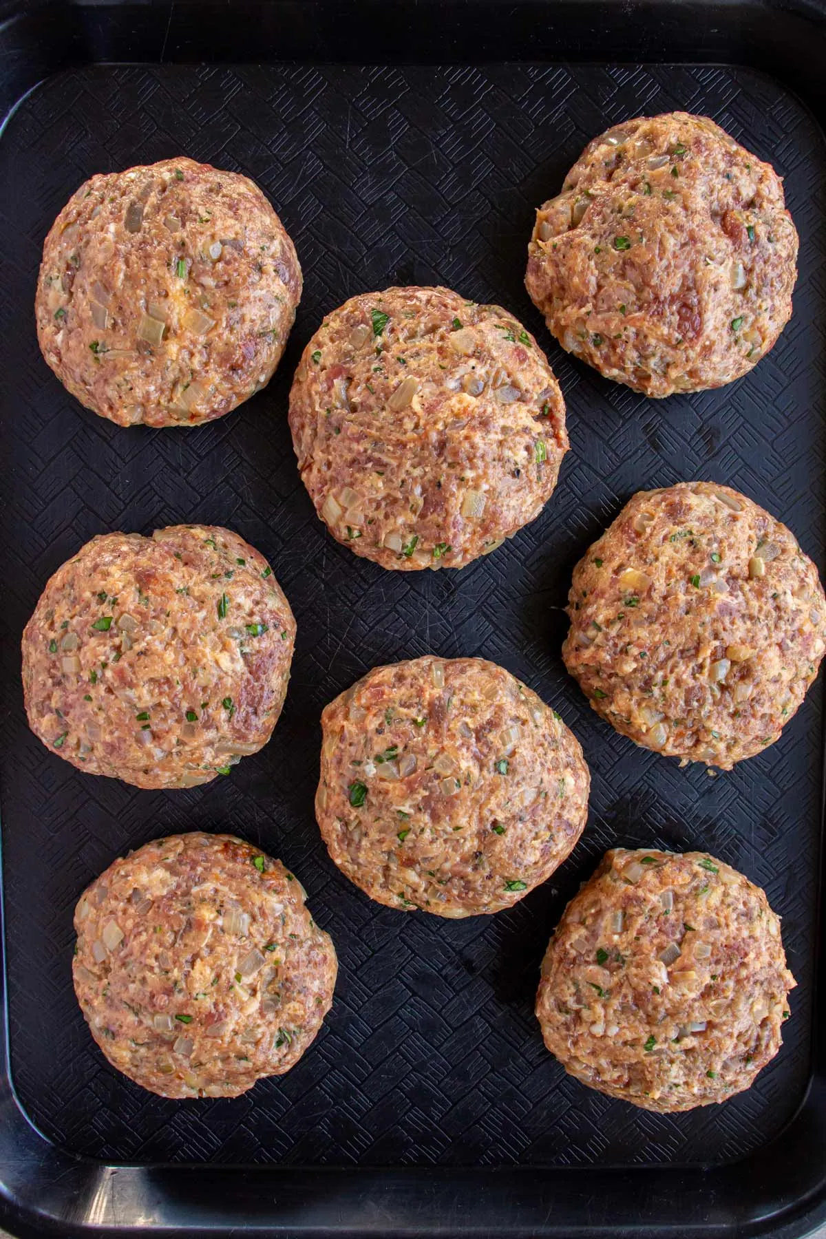 Acht roh geformte, dicke Buletten-Patties auf einem schwarzen Tablett, bereit zum Braten.