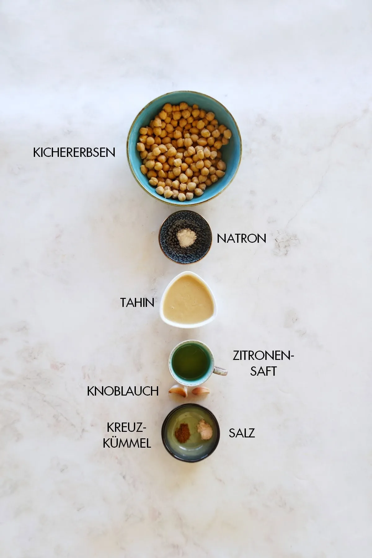 Alle frischen Zutaten für die Zubereitung von Hummus auf einem Holztisch, darunter Kichererbsen, Tahin und Zitrone