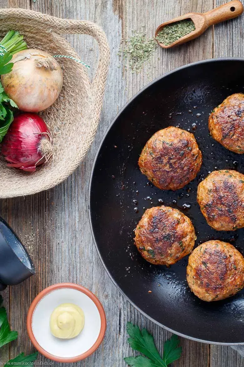 Alle notwendigen Zutaten für Buletten: Hackfleisch, Zwiebeln, Eier, Petersilie und Gewürze auf einem Holzbrett.
