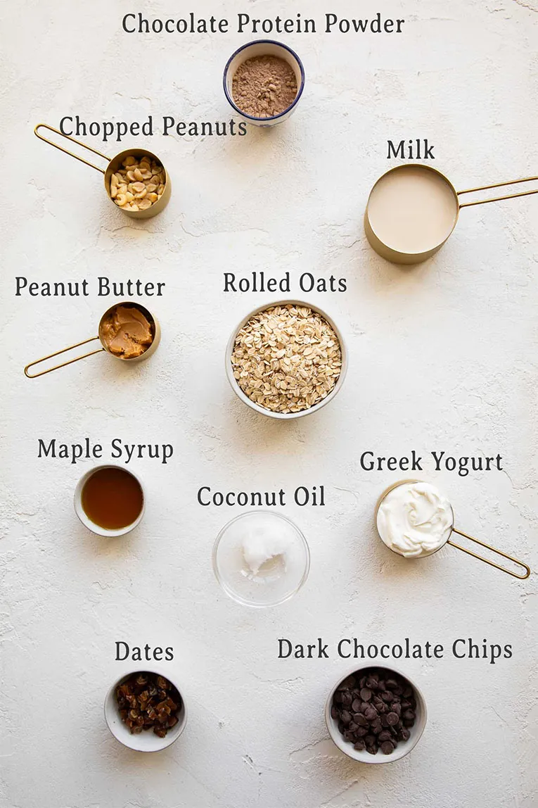 Alle Zutaten für das proteinreiche Snickers Overnight Oats Rezept, inklusive Haferflocken, Erdnussbutter und Schokolade.
