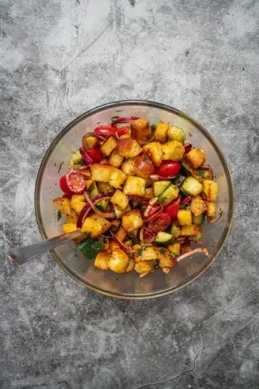 Alle Zutaten für den Panzanella: geröstetes Brot, frisches Gemüse und Dressing in einer großen Schüssel vermengen
