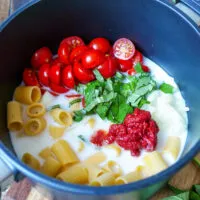 Alle Zutaten für die One Pot Pasta – Nudeln, Tomaten, Zwiebel, Knoblauch, Wasser, Sahne und Tomatenmark – bereit zum Kochen in einem Topf.