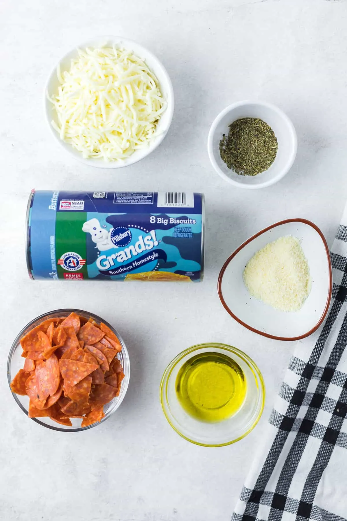 Alle Zutaten für Pizza Muffins in einzelnen Schälchen um eine ungeöffnete Dose Keksteig arrangiert.