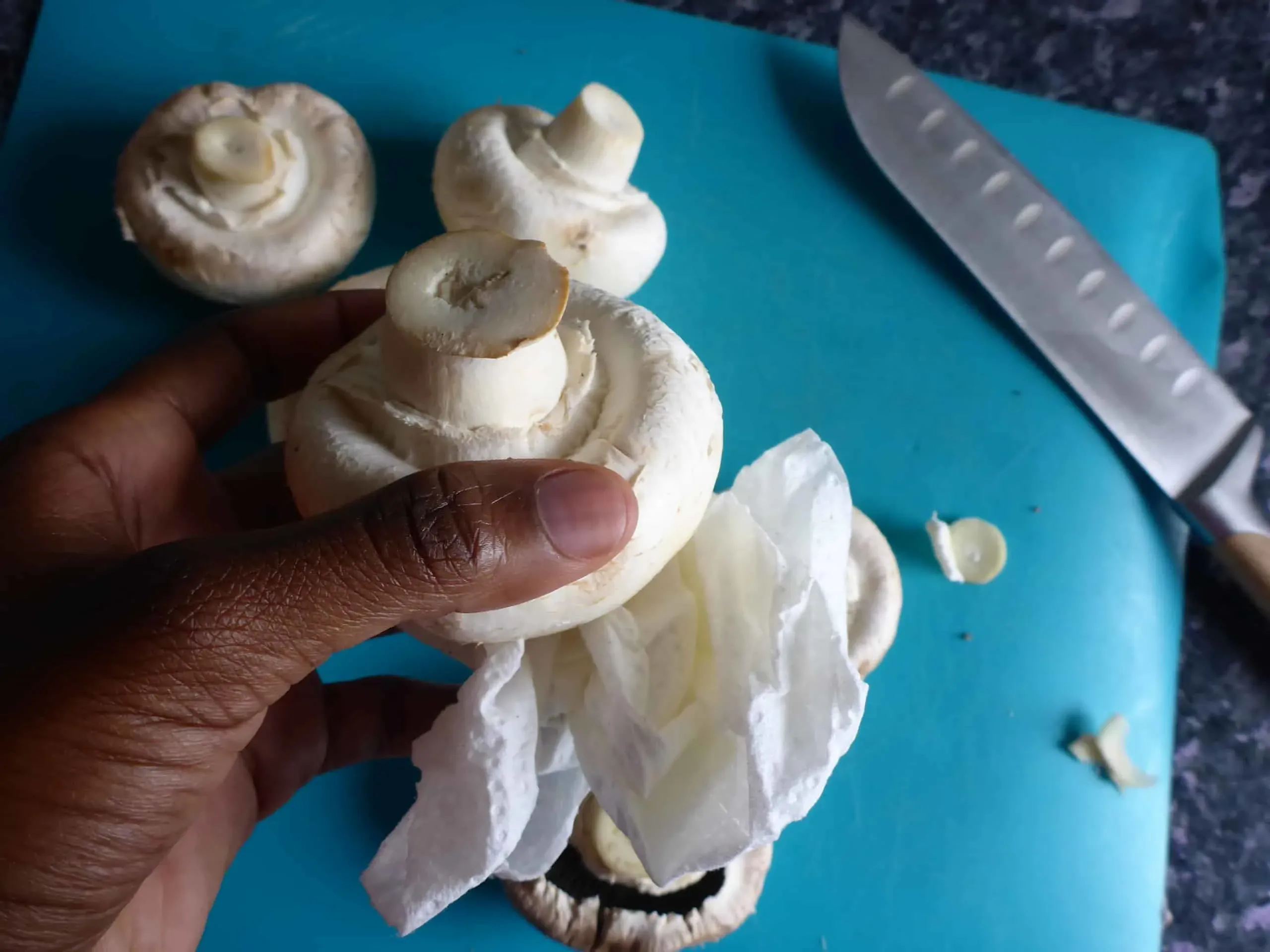Anleitung zum Putzen von Champignons: Eine Hand wischt vorsichtig eine Pilzkappe mit einem Papiertuch ab, wichtiger Schritt für die Vorbereitung der Schnitzelpfanne.