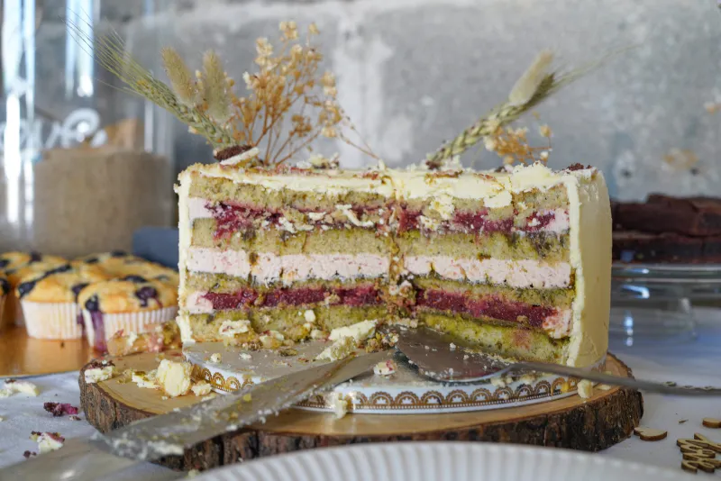 Anschnitt einer zweistöckigen Hochzeitstorte, bei der die untere Schicht mit Pistazienböden, Erdbeercreme und Fruchfüllung sichtbar ist