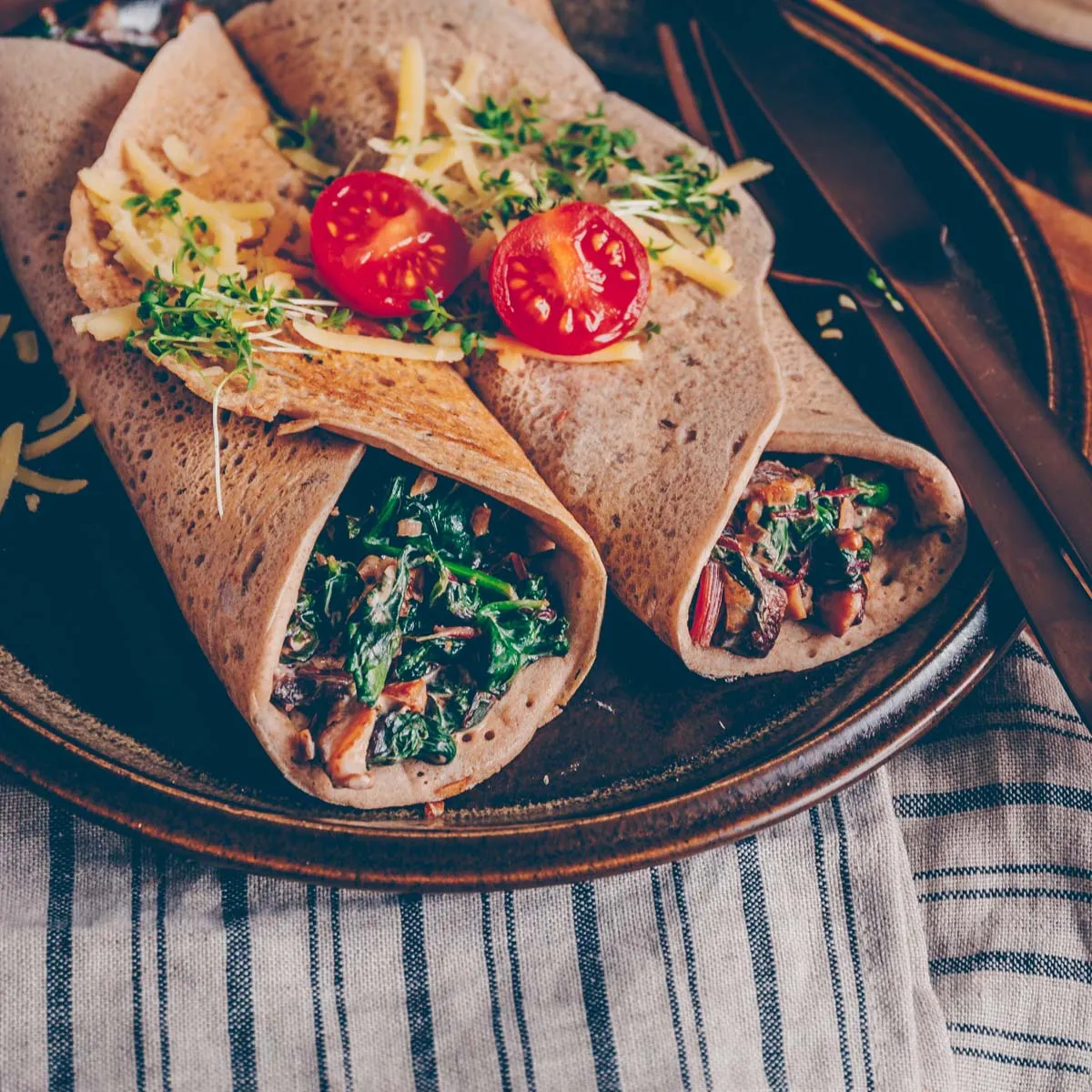 Ansicht von oben auf einen Teller mit köstlichen Buchweizenpfannkuchen, prall gefüllt mit einer herzhaften Spinatfüllung, die zum sofortigen Genießen einlädt.