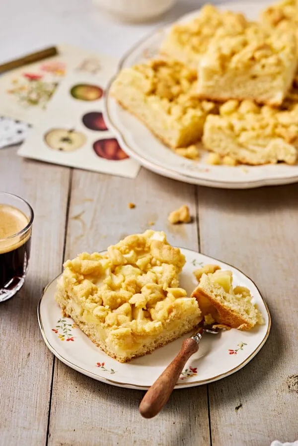 Apfelkuchen mit Hefeteig und Streusel auf einer Servierplatte mit Gedeck.