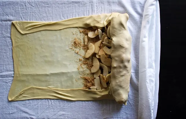 Apfelstrudel vorsichtig mit einem Tuch aufrollen, um die perfekte Form zu erhalten, wichtiger Schritt im Strudel Rezept