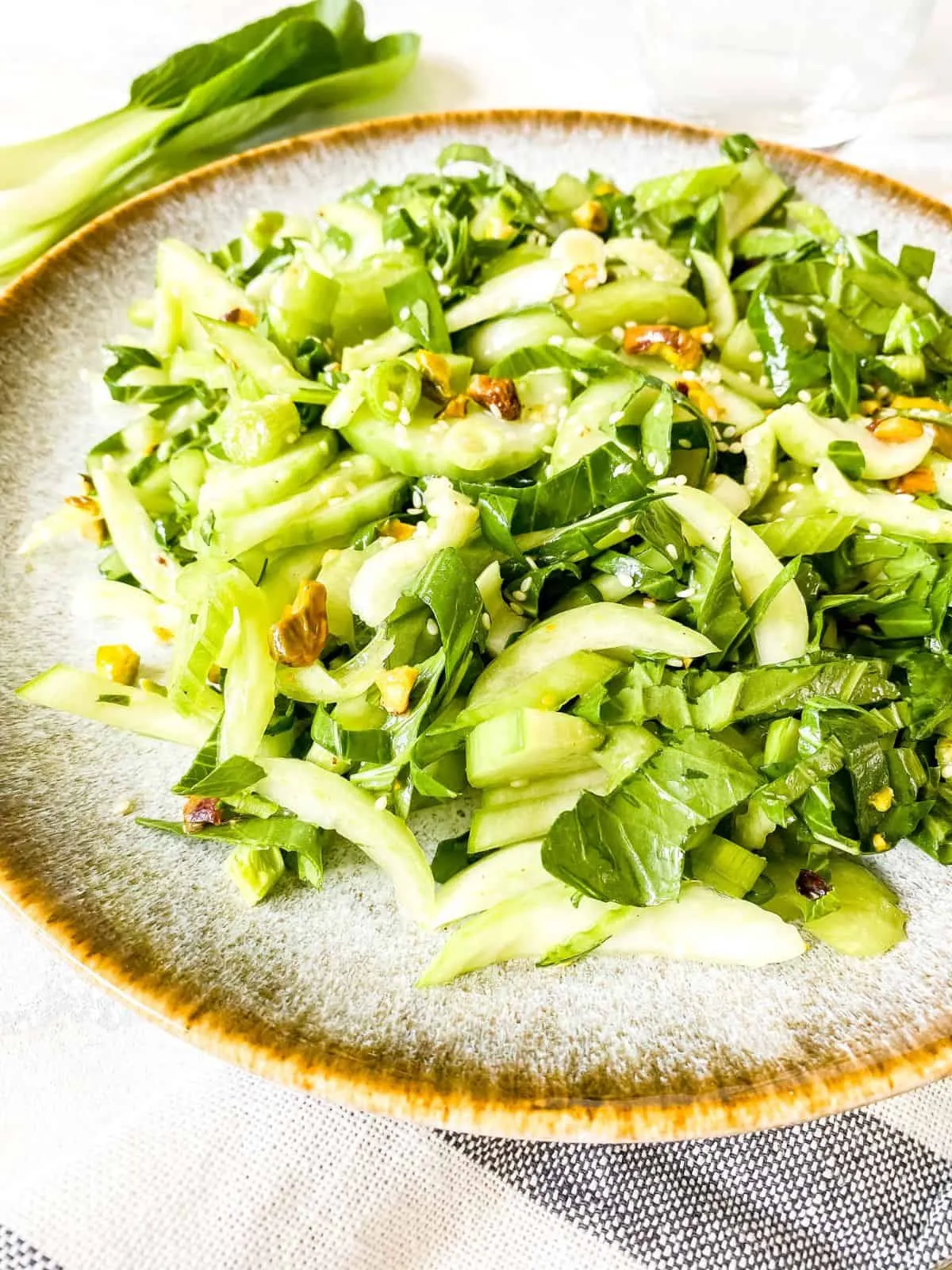 Appetitlicher Pak Choi Salat auf einem grauen Teller, mit frischem Pak Choi im unscharfen Hintergrund.