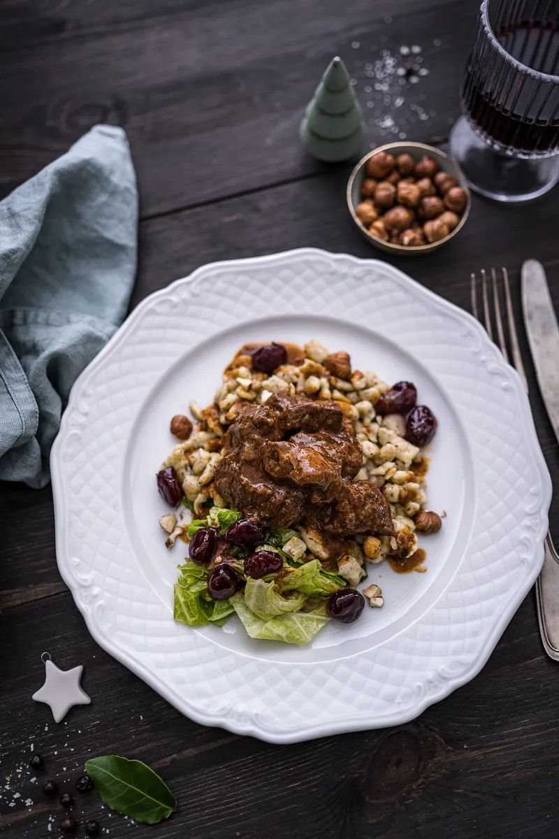 Appetitliches Foto von Wildschweingulasch mit Haselnuss-Spätzle, das die dunkle Farbe des Gulaschs und die Textur der Spätzle zeigt.