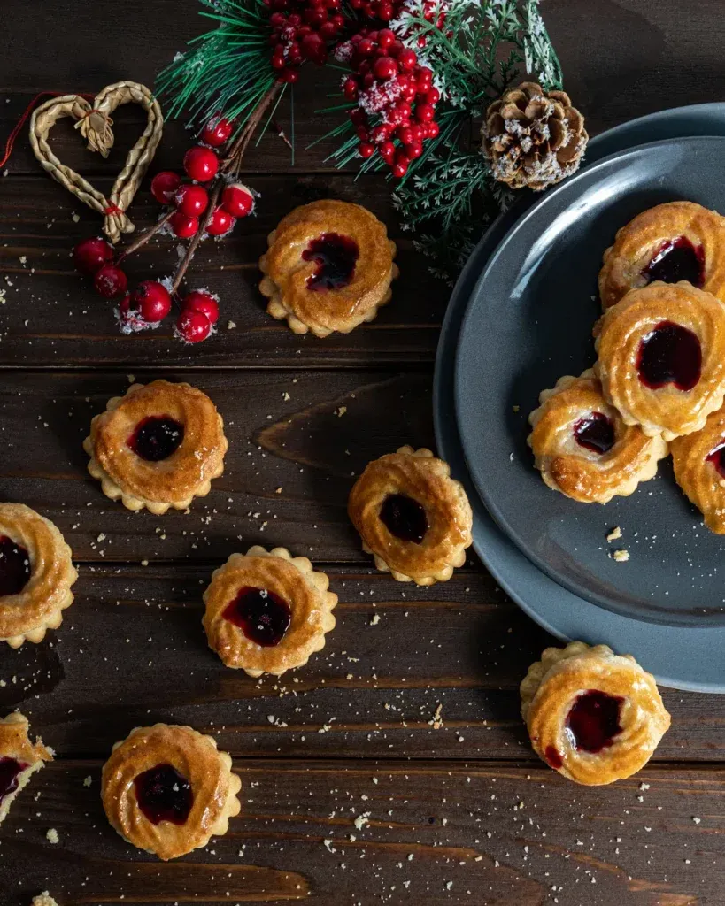Arrangement von frisch gebackenen Pfauenaugen Plätzchen auf einer Holzoberfläche, die ihre appetitliche Glasur und Füllung hervorhebt