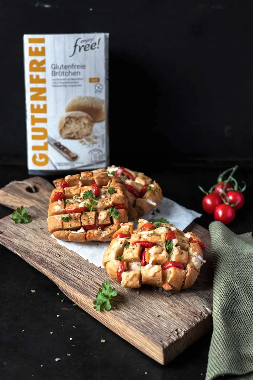 Aufgeschnittene glutenfreie Brötchen, belegt mit Butter, Schnittlauch und Käse auf einem Frühstückstisch