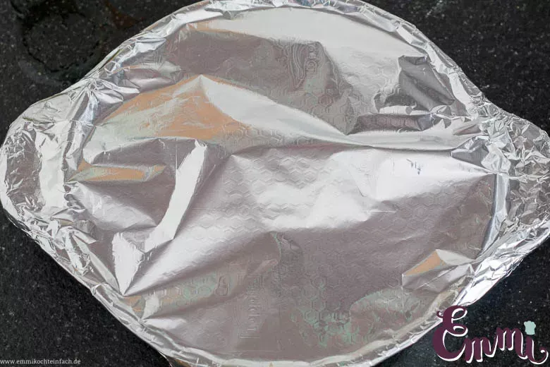 Auflaufform mit geschichtetem Zucchini-Aubergine-Gemüse, abgedeckt mit Alufolie, bereit zum Backen.