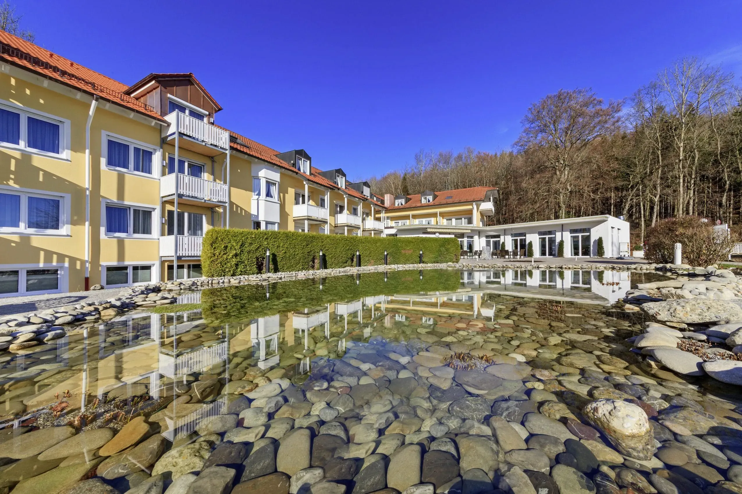 Außenansicht des Vitalhotel Sonneck in Bad Wörishofen im Herbst, mit Blick auf den Naturteich und die Hotelbalkone, ideal für einen erholsamen Urlaub mit Hund.