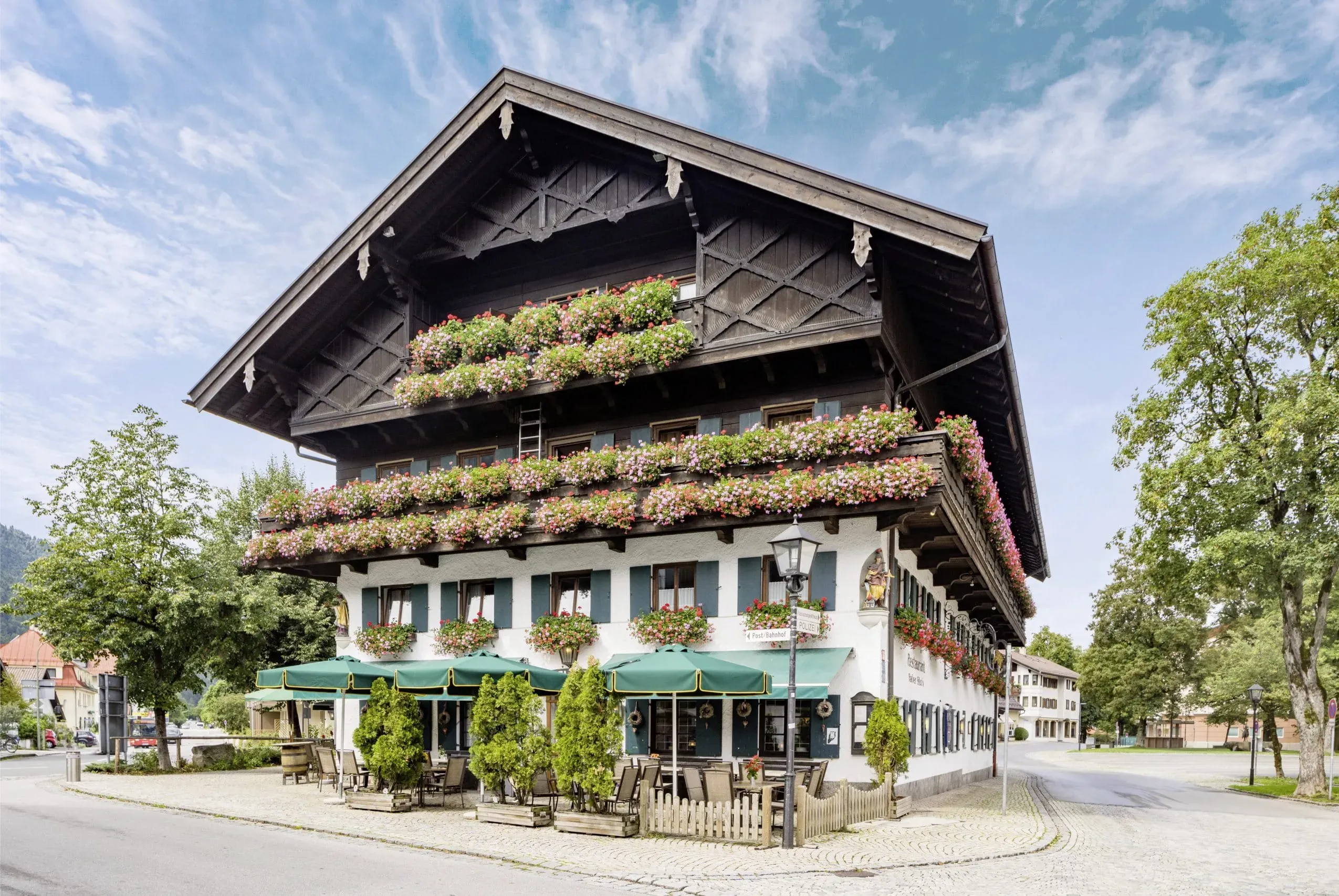 Außenaufnahme des Hundesporthotel Wolf in Oberammergau im Sommer, mit einer einladenden Terrasse und blumengeschmückten Balkonen, perfekt für Urlaub mit Hund.