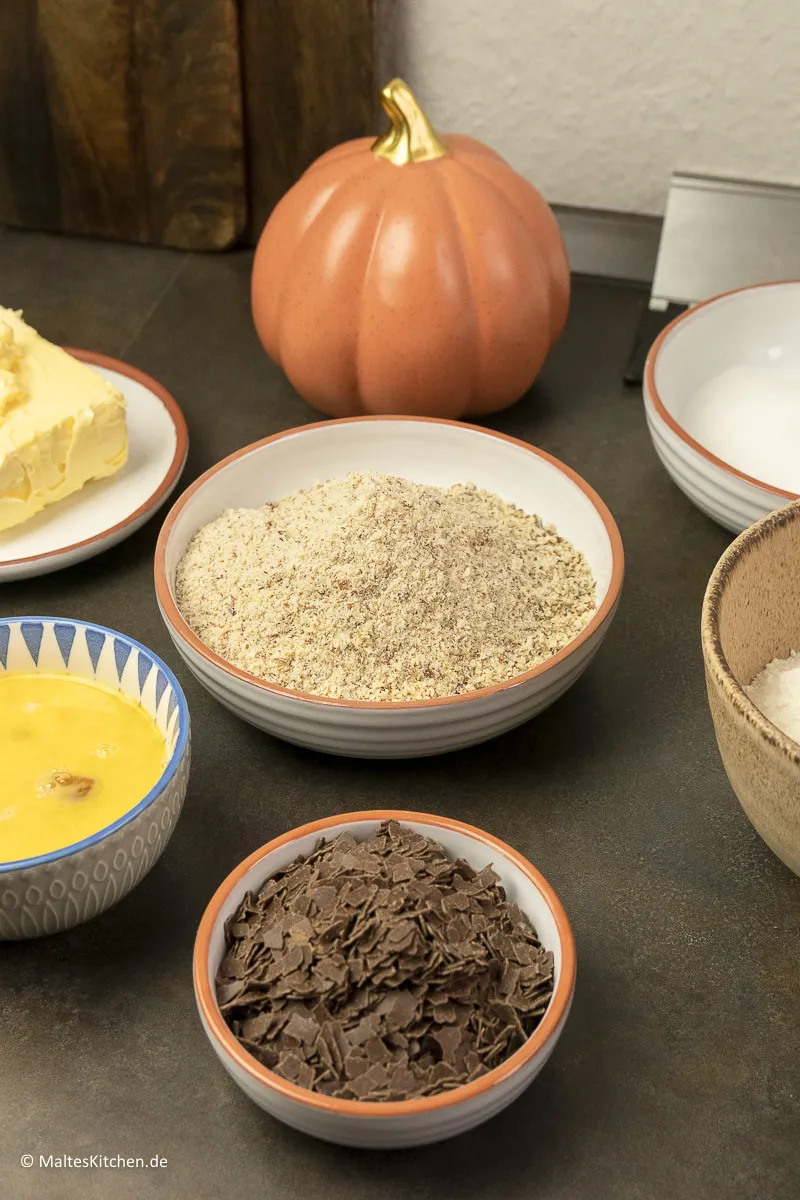 Auswahl frischer Zutaten für Omas besten Nusskuchen: Mehl, Eier, Butter, Haselnüsse und Schokoladenraspeln bereit zum Backen.