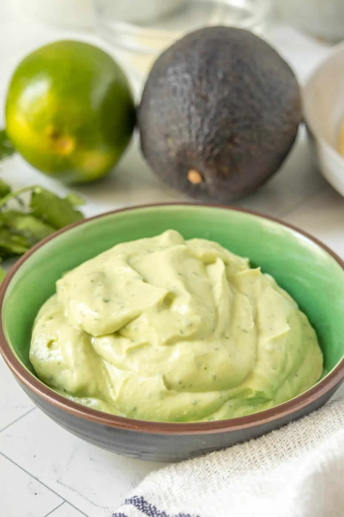 Avocado Creme in einer Schale mit Limetten und weiteren Zutaten.