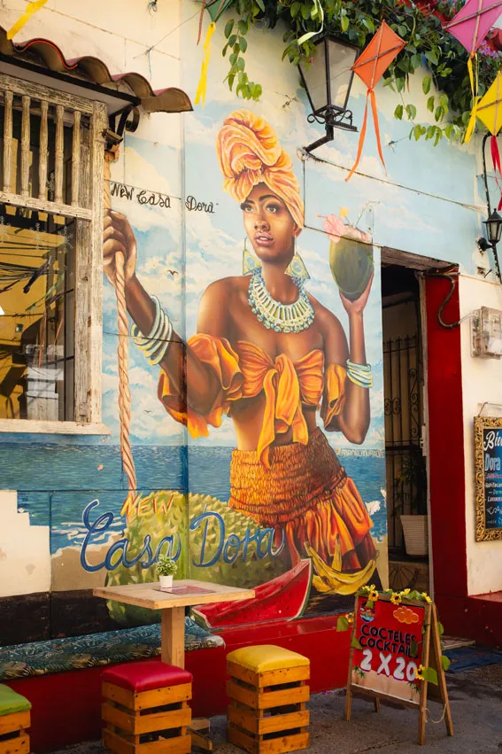 Bar mit Hockern vor einem Wandgemälde einer Frau mit Trinkkokosnuss