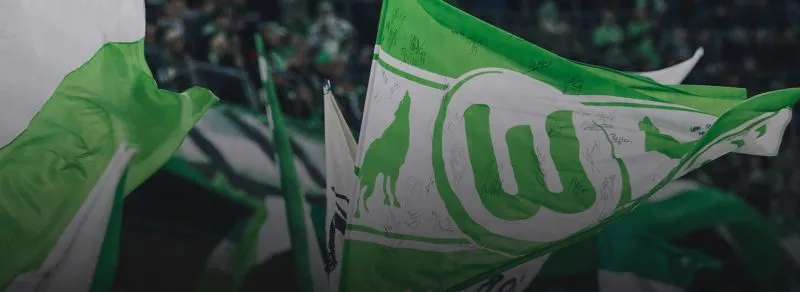 Begeisterte Fans des VfL Wolfsburg schwenken grün-weiße Fahnen im Stadion, eine Szene, die die leidenschaftliche Bundesliga-Atmosphäre in Deutschland widerspiegelt.