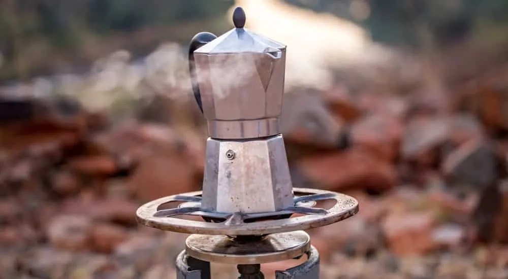 Bialetti Espressokocher auf einem Campingkocher mit Standblech, zubereitend aromatischen Mokka für den Outdoor-Genuss.