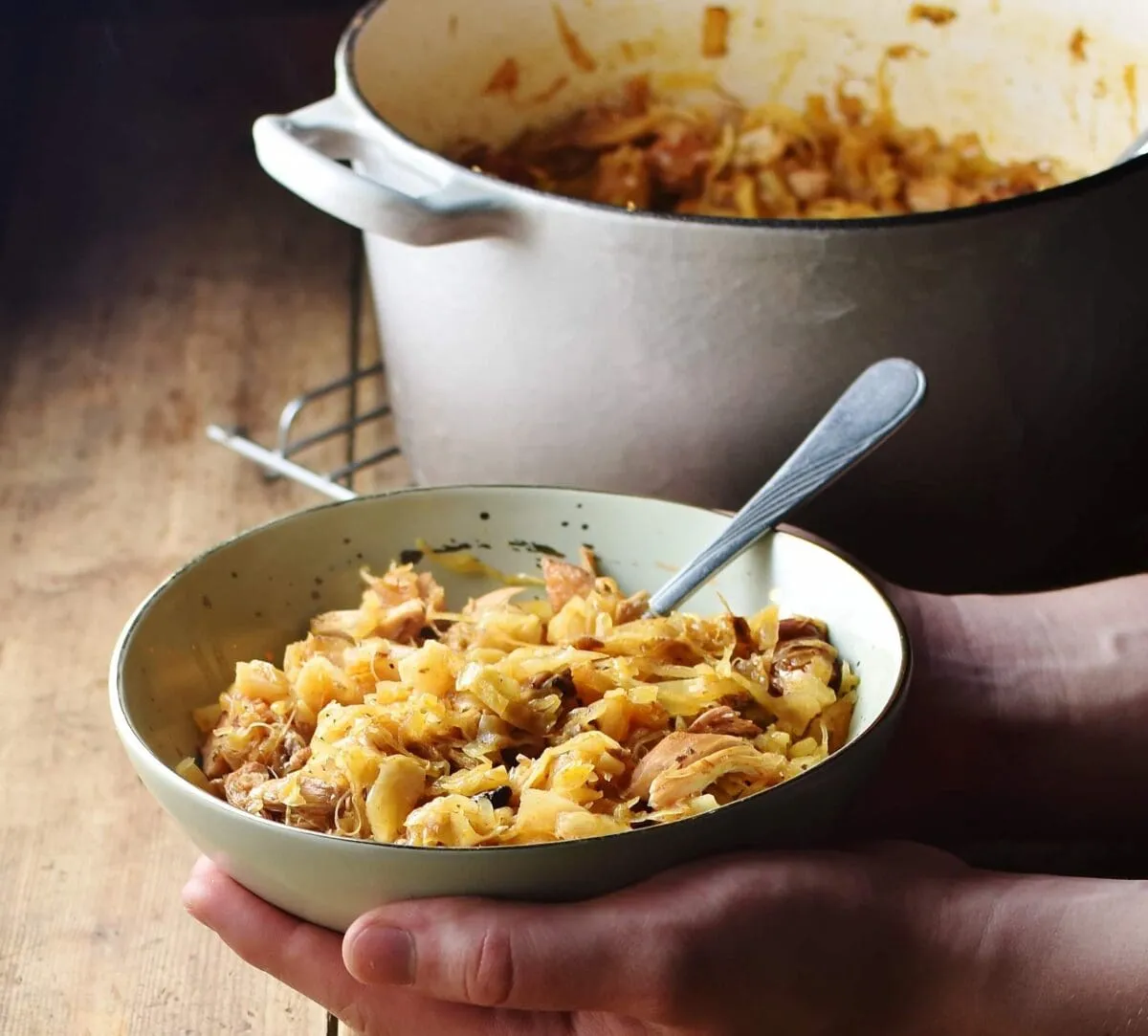 Bigos-Eintopf in grüner Schale mit Löffel, im Hintergrund ein großer Topf mit schwelendem Krauteintopf