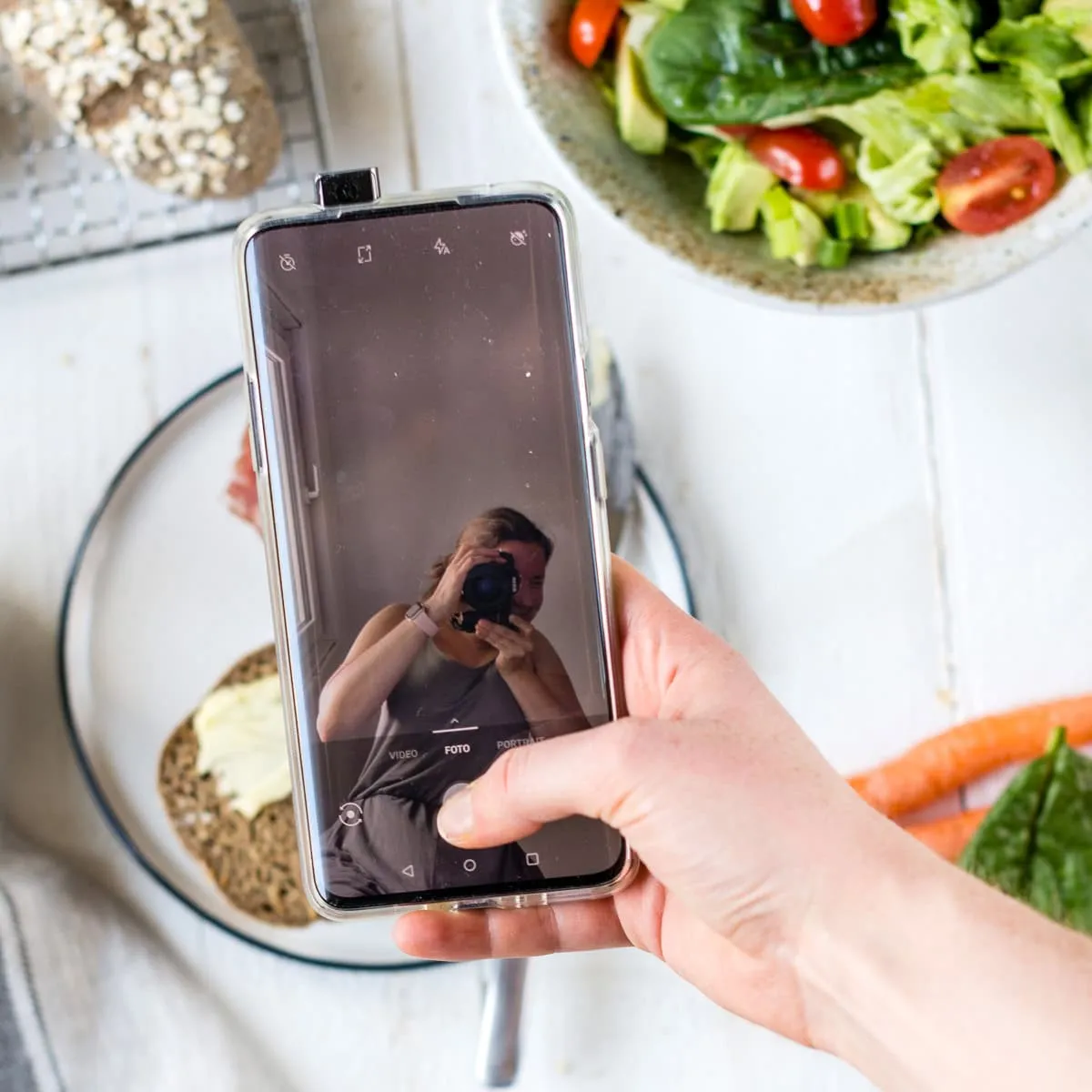 Blick hinter die Kulissen: Ein Smartphone mit geöffneter Kamera-App auf einem gedeckten Tisch, das die Entstehung unserer besten reinen Haferbrötchen dokumentiert.