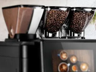 Blick in den Bohnenbehälter eines Kaffeevollautomaten, gefüllt mit frischen Kaffeebohnen, bereit für die Zubereitung