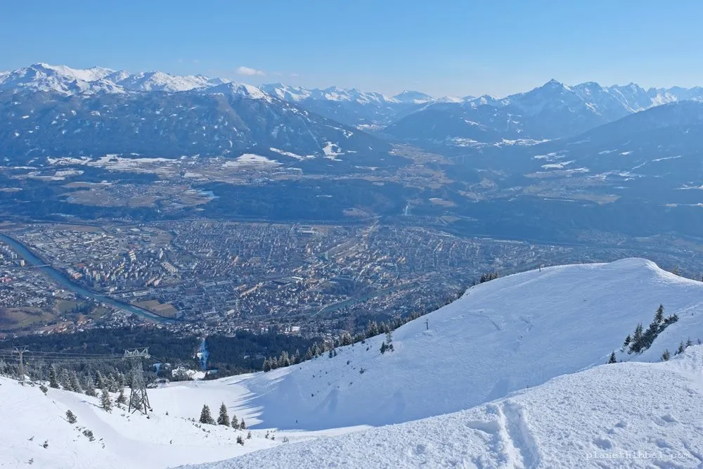 Blick vom Gipfel auf verschneite Berge und Stadt im Tal