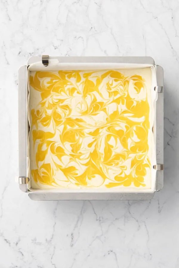 Blick von oben auf eine Backform mit Käsekuchenriegeln und eingeschwenktem Lemon Curd vor dem Backen.