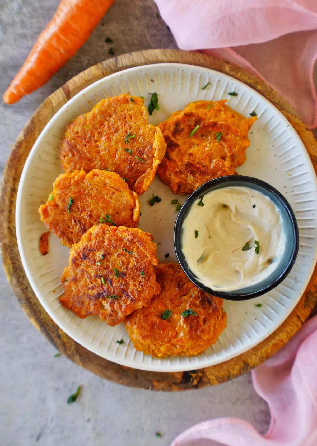 Blick von oben auf goldbraune Karotten-Puffer und einen cremigen Dip