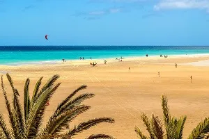 Breiter Sandstrand auf Fuerteventura, Kanarische Inseln, mit klarem Wasser und Windsurfern, perfekt für Juli-Urlaub.