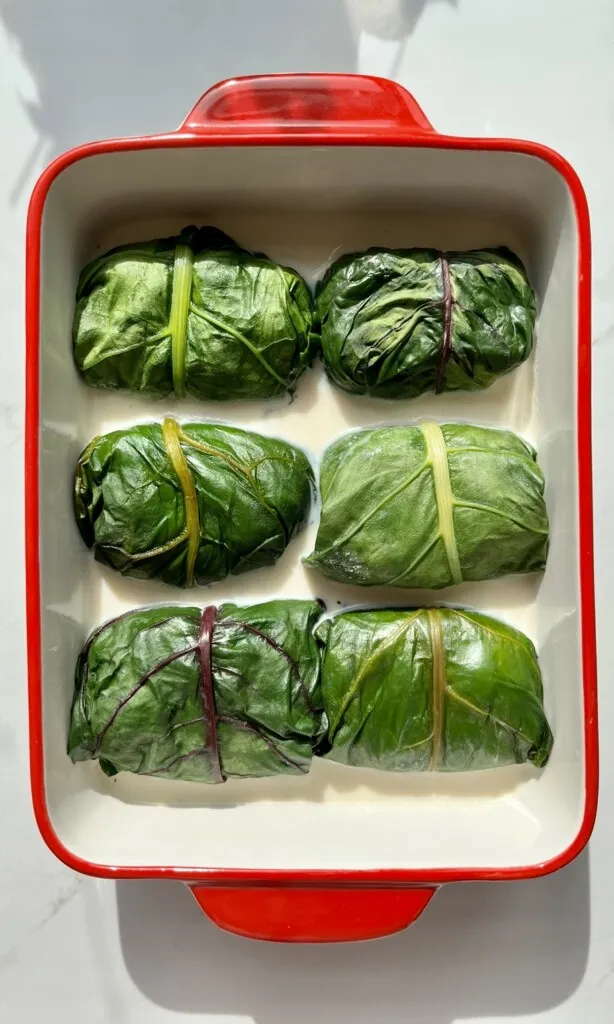 Bündner Capuns servierfertig auf einem Teller mit geriebenem Käse und Salsiz.