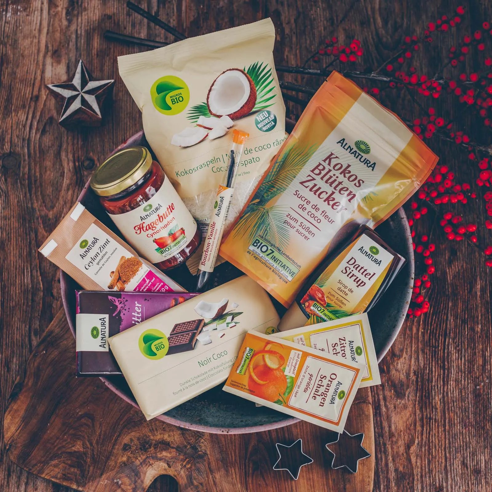 Bunte Auswahl an veganen Plätzchen, darunter Konfitüre-Rollen, Karamell-Cookies und Kokos-Sterne, ansprechend arrangiert auf einem Holzbrett