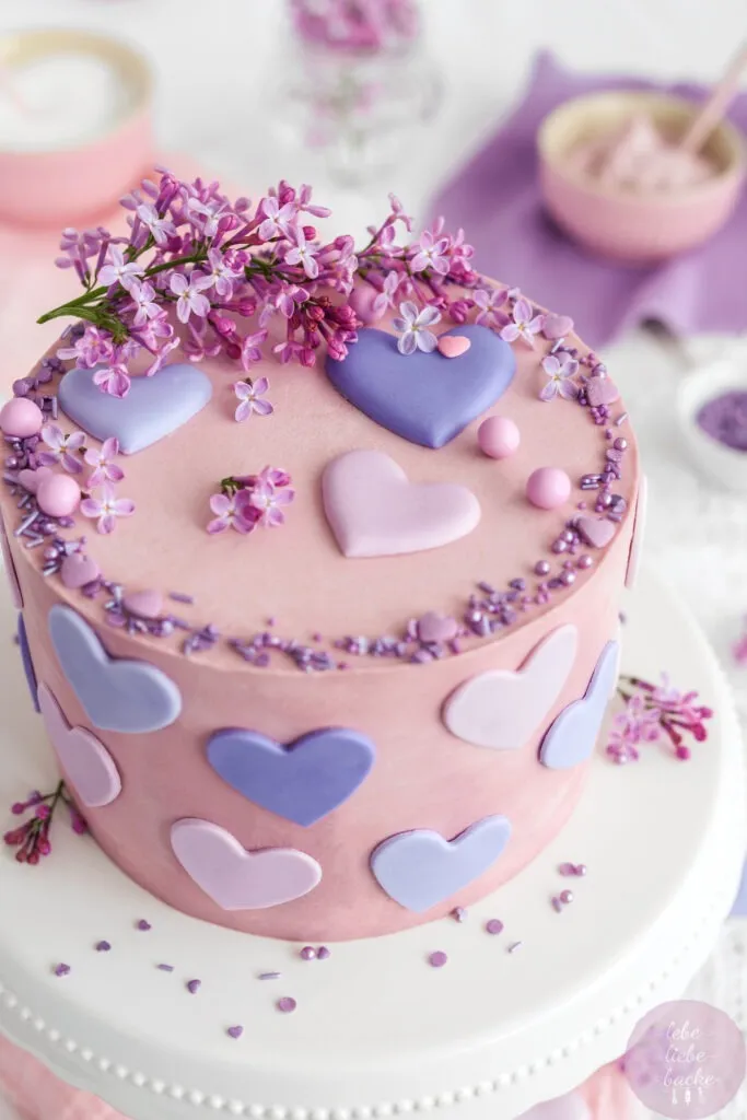 Bunte Geburtstagsdekoration auf der Käse-Sahne-Torte mit rosa Buttercreme und frisch gepflücktem Flieder