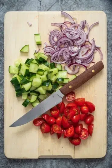 Bunte Kirschtomaten, frische Gurken und rote Zwiebeln werden für den Panzanella Brotsalat geschnitten