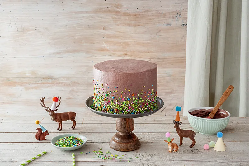 Bunte Streusel werden auf den unteren Rand des Geburtstagskuchens Waldtiere gestreut