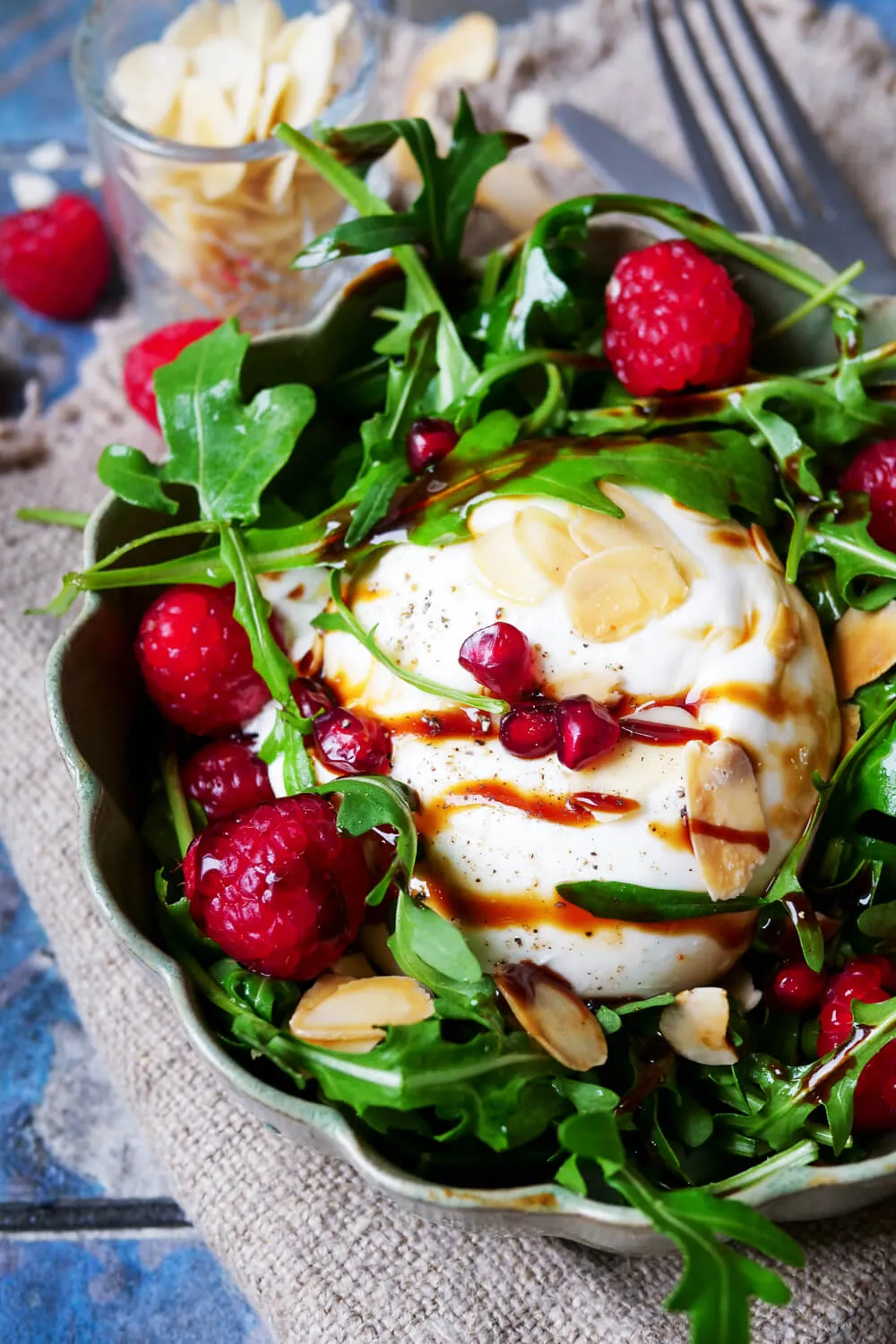 Burrata-Salat mit Himbeeren und Granatapfelkernen auf einem Teller.