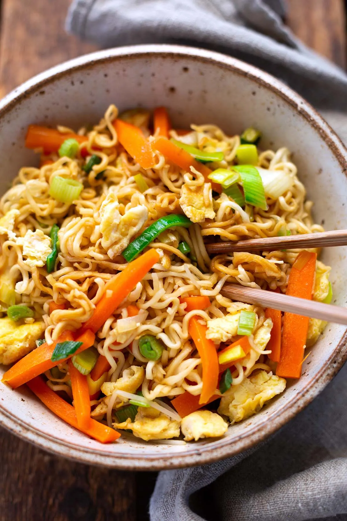 Chinesisch gebratene Nudeln mit viel Gemüse und Ei, ansprechend in einer Schüssel angerichtet und mit Essstäbchen serviert.