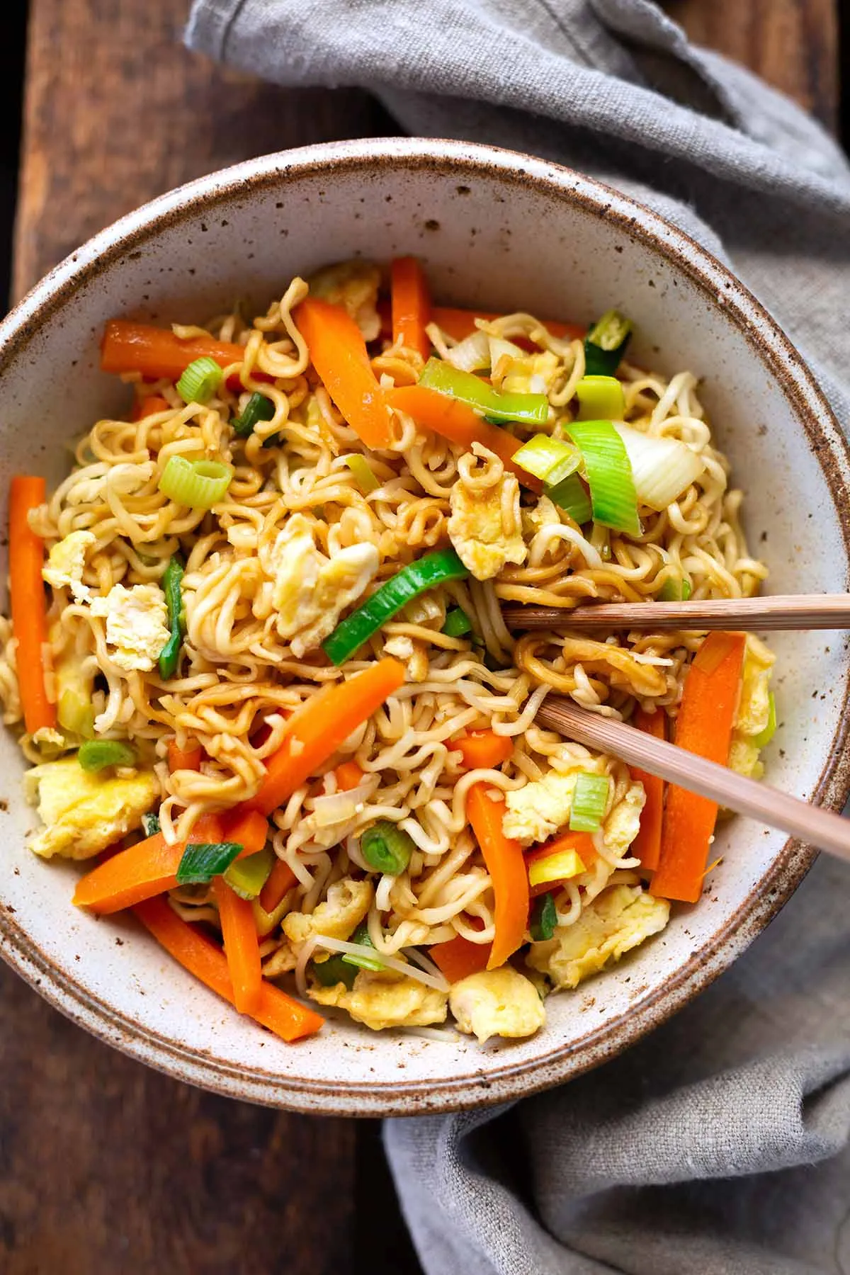 Chinesisch gebratene Nudeln mit viel Gemüse und Ei, appetitlich in einer Schüssel angerichtet und servierfertig mit Essstäbchen.