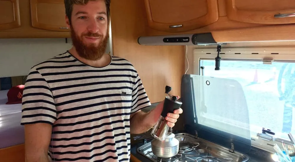 Christian von Happy Coffee mahlt mit der Hario Skerton Handkaffeemühle frische Bohnen in einem Wohnmobil in England, perfekt für eine Reise Kaffeemaschine.