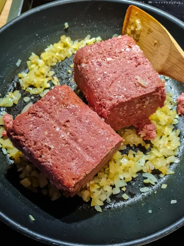 Corned Beef zu gebratenen Zwiebeln in der Pfanne geben