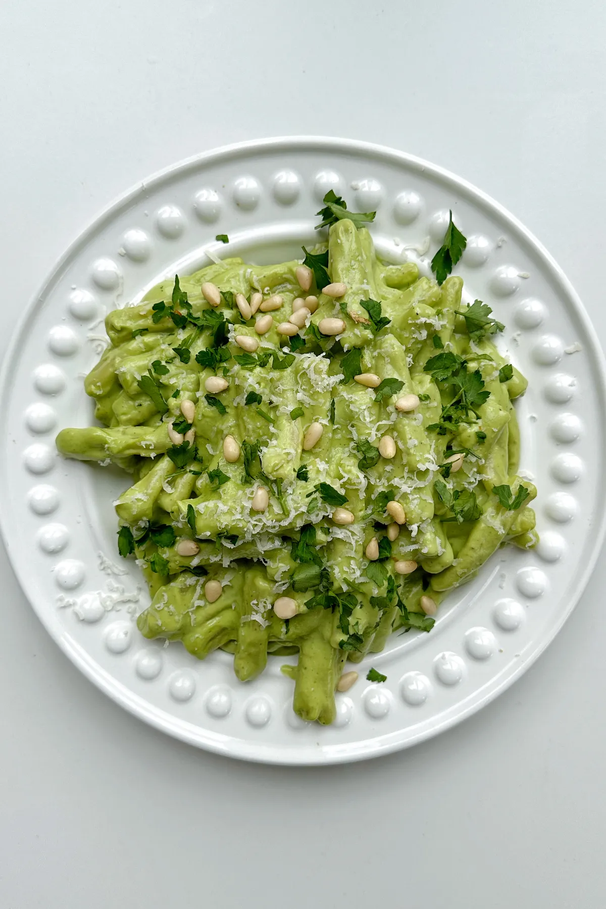 Cremige Avocado Pesto Pasta auf einem weißen Teller, garniert mit Pinienkernen und frischem Basilikum.