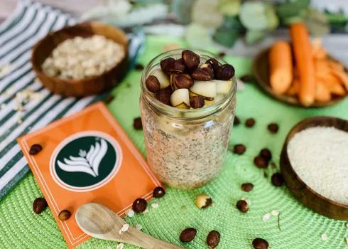 Cremige Karotten-Overnight-Oats in einem Glas mit Nüssen und frischen Karottenraspeln