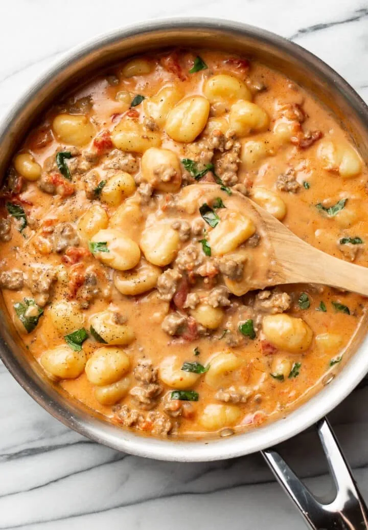 cremige One-Pot-Gnocchi mit Wurst in der Pfanne, servierbereit mit Holzlöffel