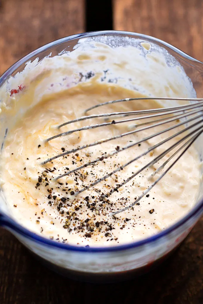 Cremige Sahnesauce für den Brokkoli-Nudelauflauf mit einem Schneebesen in einem Glasmessbecher gerührt, bereit für die Zubereitung.