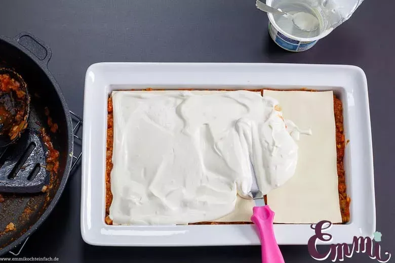 Cremige Schmand-Schicht wird gleichmäßig auf der Gemüselasagne verteilt, für eine saftige Konsistenz