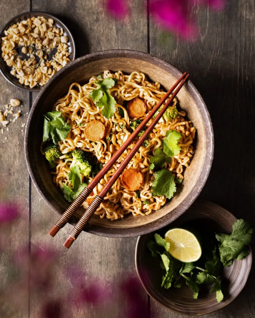 Cremige vegane Erdnussnudeln in einer Schüssel mit frischem Koriander und Limettenspalten