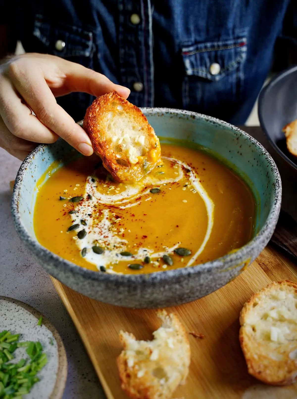Cremige vegane Kürbissuppe mit herbstlichen Aromen, in die ein Stück Brot eingetaucht wird, ein wohltuendes Mittagessen.