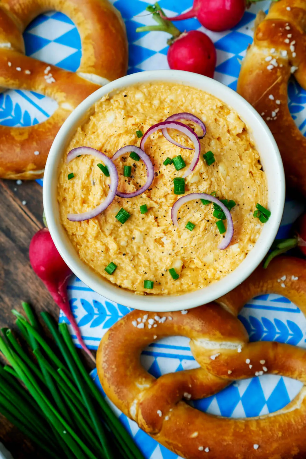 Cremiger Obazda in einer Schüssel, garniert mit Schnittlauch, daneben frische Brezn für eine traditionelle Brotzeit