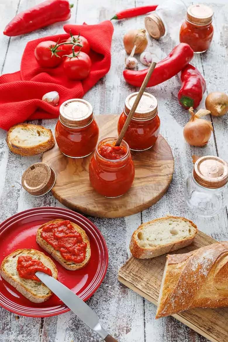 Cremiges Ajvar in einer Schale, daneben geröstete Paprika und Tomaten, als Basis für das Rezept